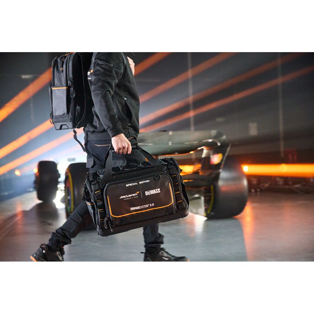 Person carrying a DEWALT ToughSystem 2.0 tool bag, with a car and orange lights in the background.